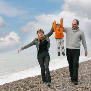 A family walking on the beach with their arms in the air.