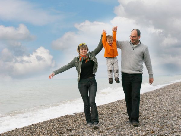 A family walking on the beach with their arms in the air.