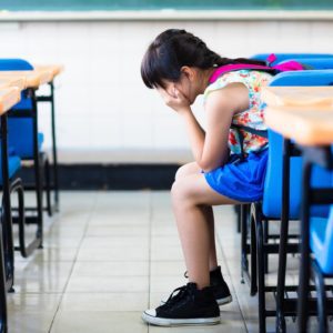 A little girl sitting on the floor of an empty classroom.