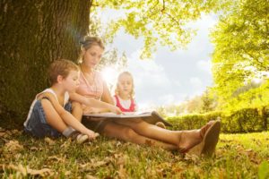 A woman and two children sitting in the grass reading.